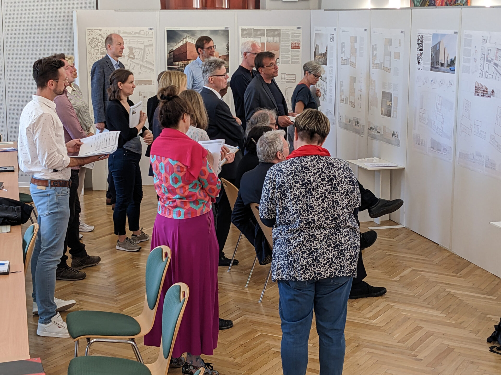 mehrere Personen stehen vor Leinwändene an denen architektonische Entwürfe angebracht sind
