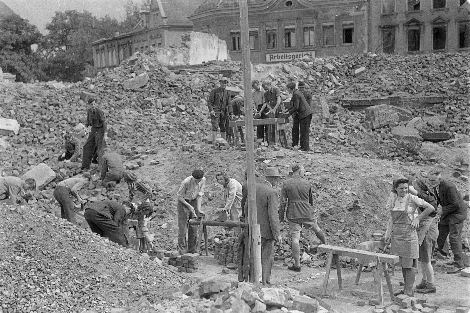 čorno-běła fotografija, na kotrejž je widźeć, kak wjacori ludźo rozwaliny rumuja