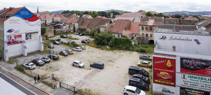 Foto aus der Vogelperspektive auf eine Anordnung von alten Gebäuden, die einen Parkplatz mit Autos säumen